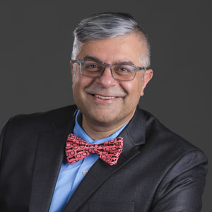Amit Taneja in a dark gray suit with a red bow tie and glasses