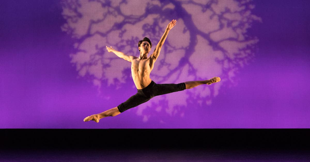 A dancer leaping in the air in front of a purple background