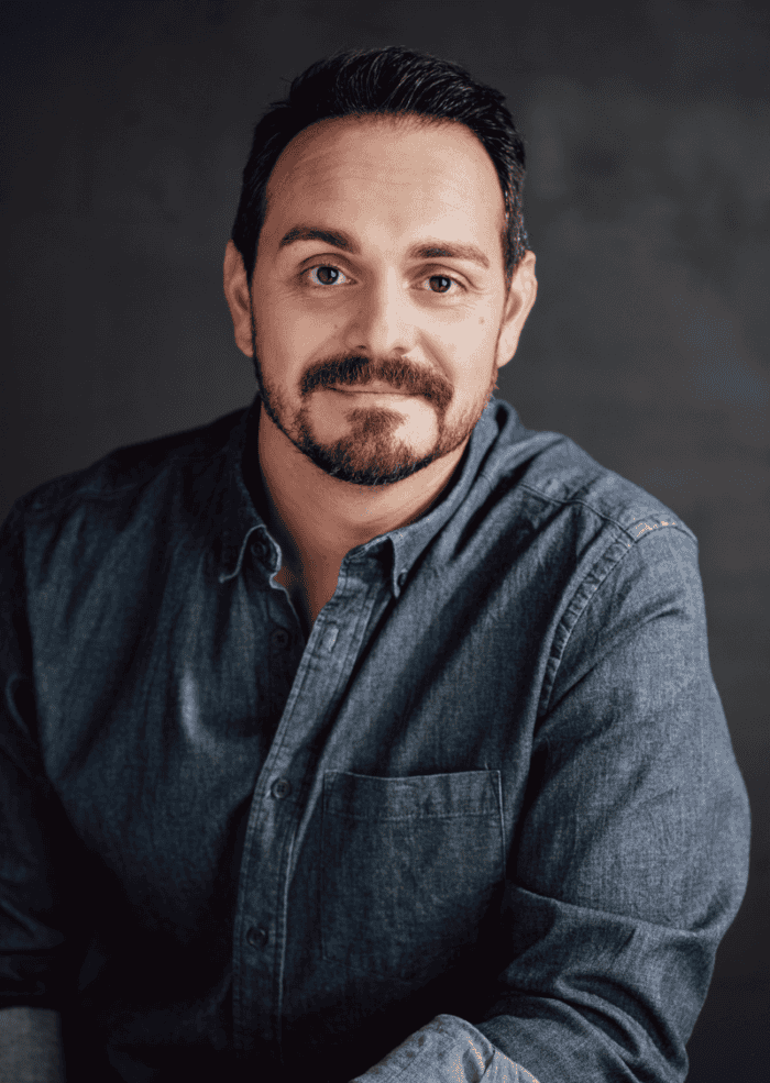 Adriano Gatto headshot. Man wearing gray shirt while he smiles facing straight ahead. 