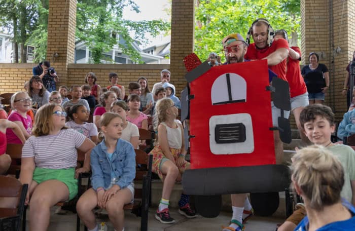 Actors dressed as a fire truck walking through a crowd of students