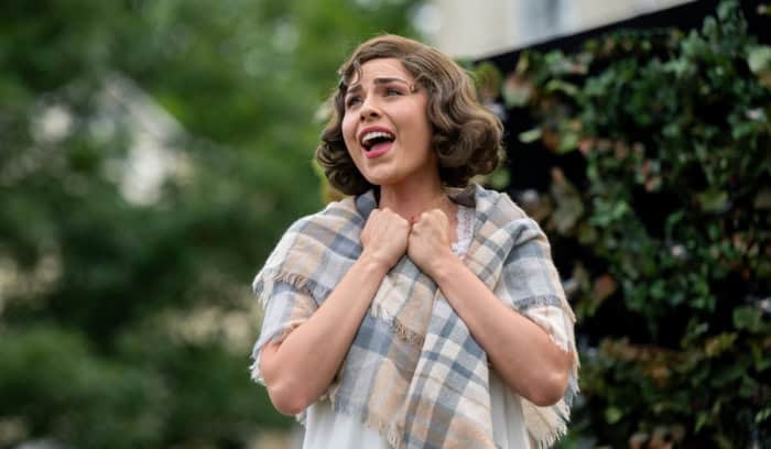 An opera singer holding her hands up to her chest as she sings