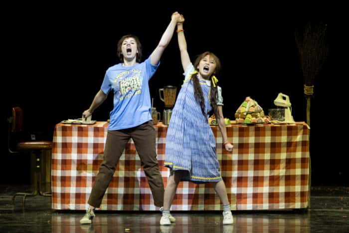 Two opera singers holding their hands up in front of a table during a production of Hansel and Gretel