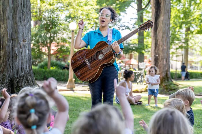 A children's school teacher playing guitar for kids in a park