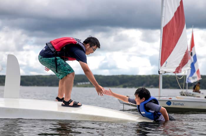 An adult helping a child out of the water during a sailing lesson