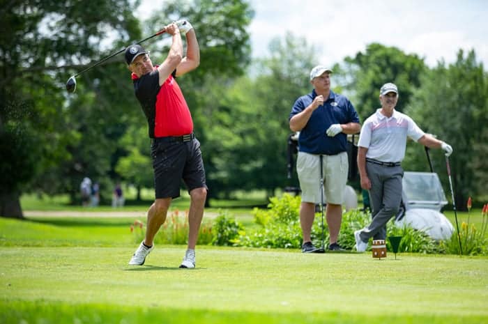 A man swinging a golf club while two other men watch