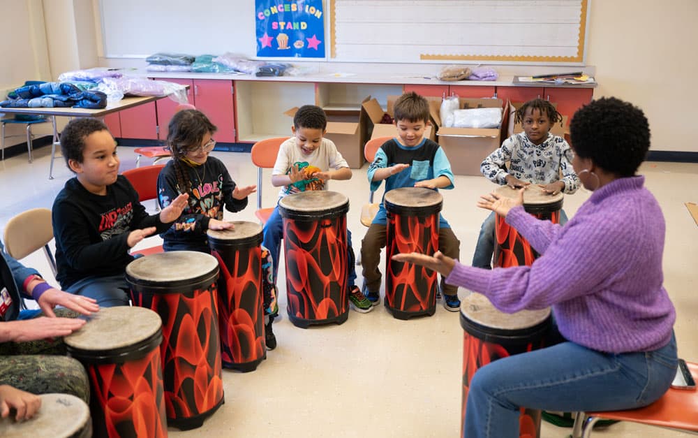 Students lined up and drumming with teaching artist Stephanie Dawson