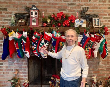 A woman standing in front of a mantel filled with stockings and decorations