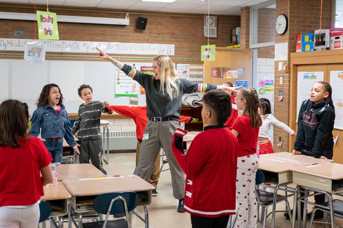 An actor and students standing in a classroom with their arms raised