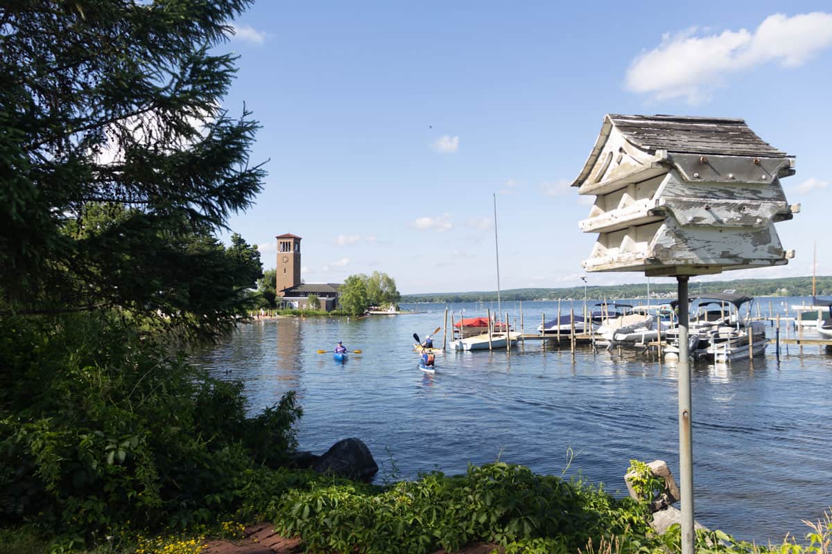 A bird house by the lake with kayakers and boats in the background