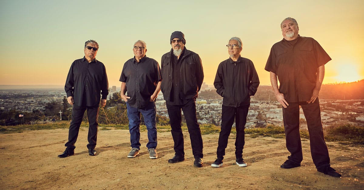 Los Lobos band standing in front of a city sunset