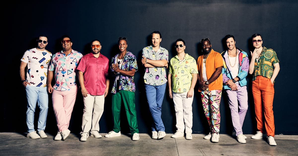 Straight No Chaser members standing in a line in colorful outfits